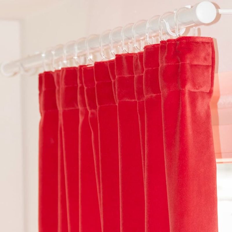 tende-acustiche-fonoassorbenti-fettuccia-autoarricciante Tenda in velluto rosso con pieghe fitte da fettuccia arricciante, appesa con anelli trasparenti a un bastone bianco