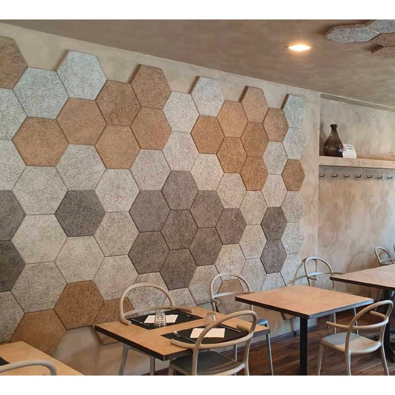 Parete rivestita di pannelli esagonali in fibra di legno nei toni beige e marrone, in una sala con tavoli